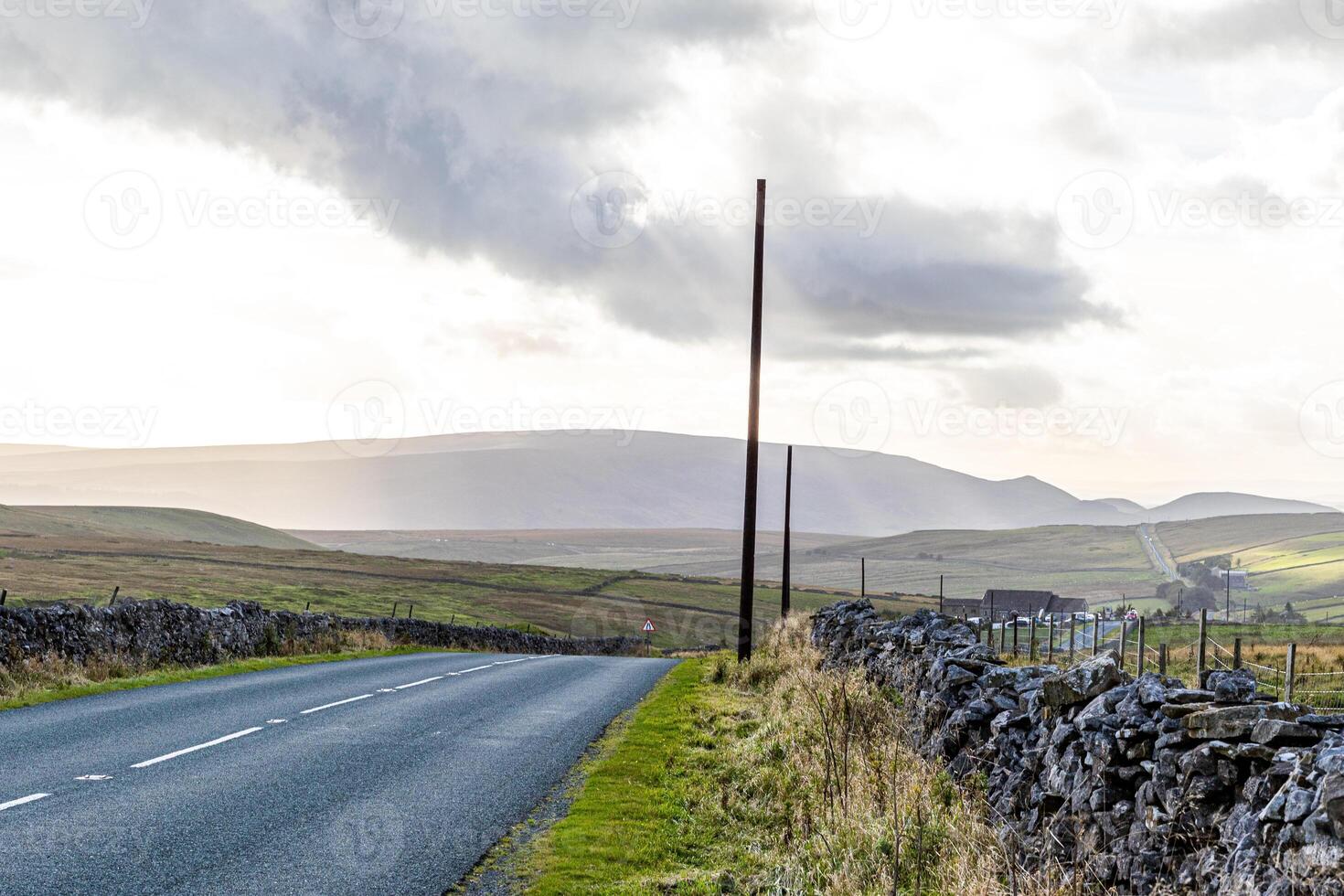 tömma landsbygden väg med en telefon Pol, sten väggar, och rullande kullar under en molnig himmel i yorkshire dalar. foto