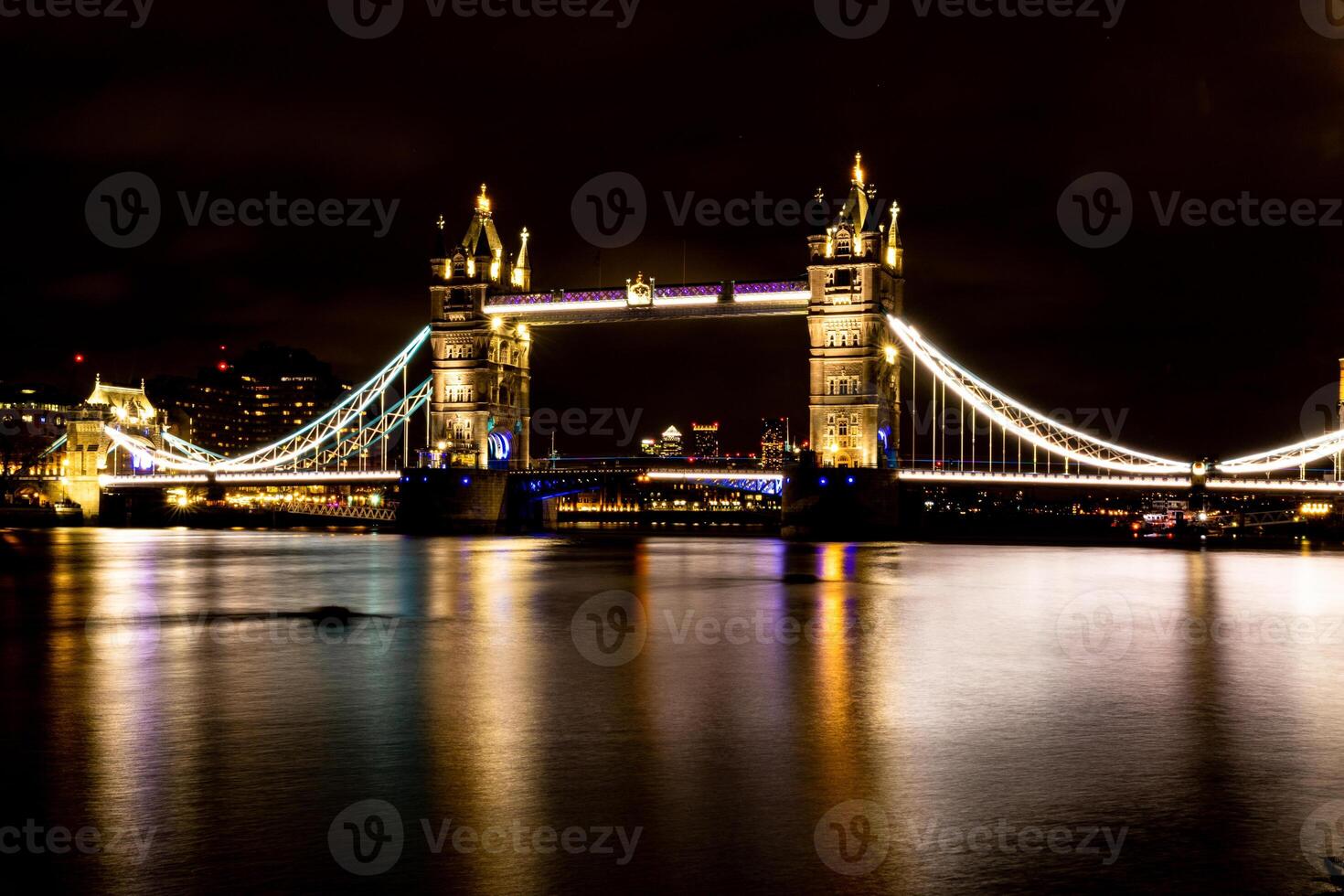 upplyst suspension bro över flod på natt med reflektioner på vatten. foto
