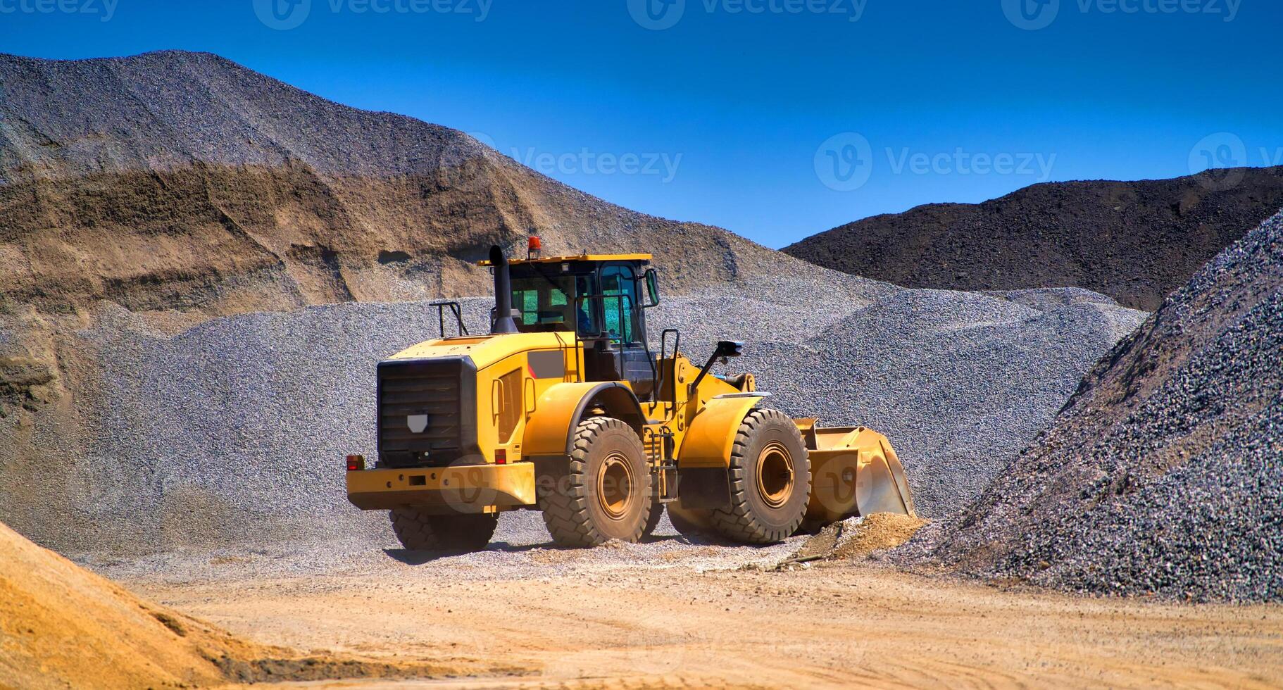 underhåll av gul grävmaskin på en konstruktion webbplats mot blå himmel. repeterar hjul lastare på sandlåda under schaktning Arbetar foto