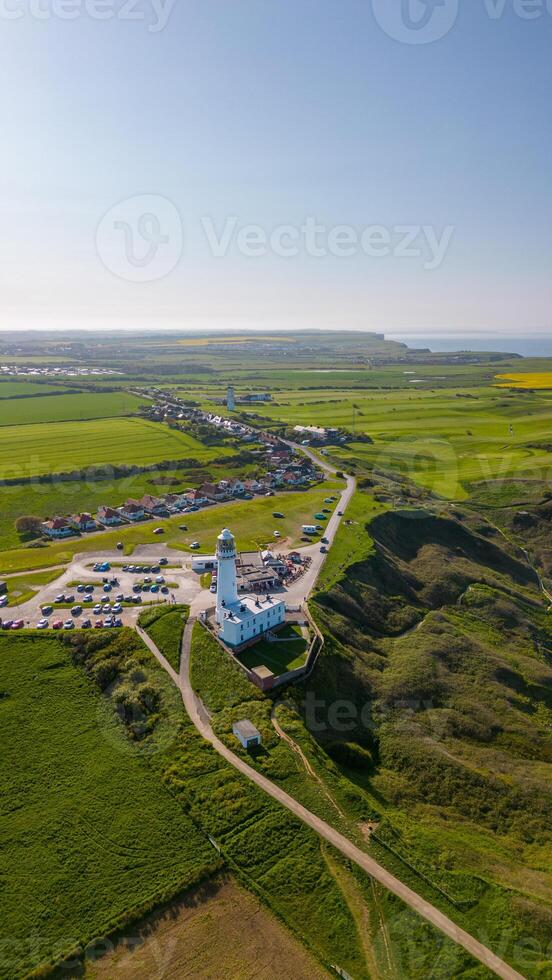 antenn se av en fyr med intilliggande byggnader omgiven förbi grön fält under en klar blå himmel i Flamborough, England foto