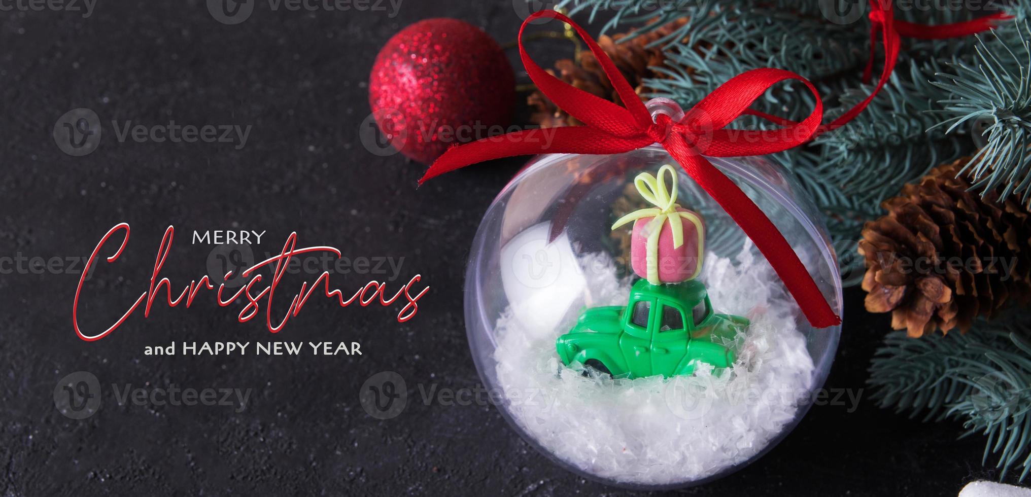god jul på mörk bakgrund med genomskinlig julboll med en leksaksbil present på taket i snön foto
