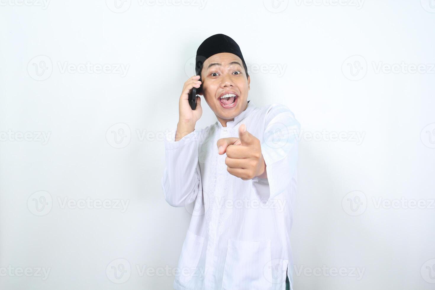 Lycklig muslim asiatisk man utseende överraskad medan talande på de telefon med pekande hand foto