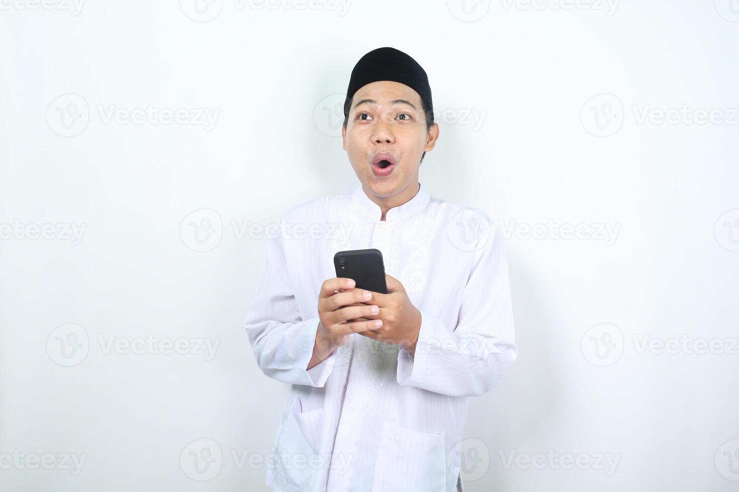 chockade asiatisk muslim man ser bort med innehav mobil telefon isolerat foto