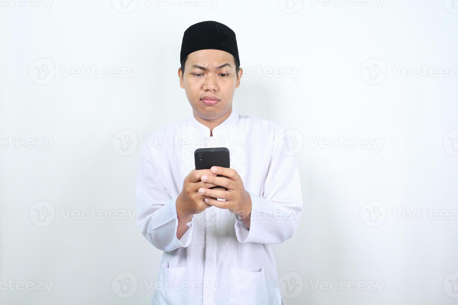 allvarlig muslim asiatisk man tittar på mobil telefon med förvirrad uttryck isolerat på vit bakgrund foto