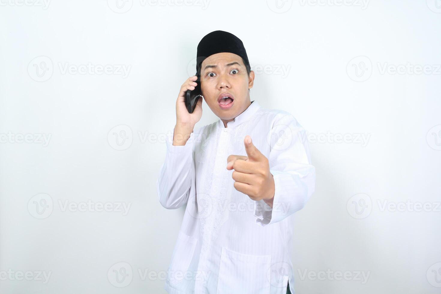 chockade asiatisk muslim man pekande på kamera medan talande på mobil telefon foto