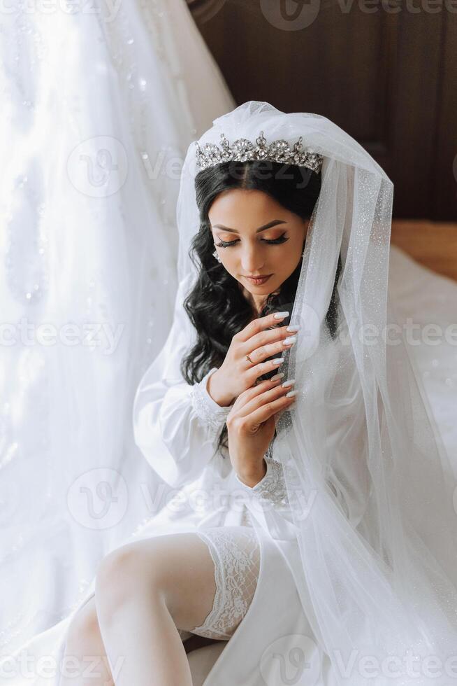 skön brud i en klä på sig klänning i de morgon- innan de bröllop ceremoni. otrolig frisyr av de brud. naturlig och modern smink. porträtt av en ung brud i en klä på sig klänning. foto