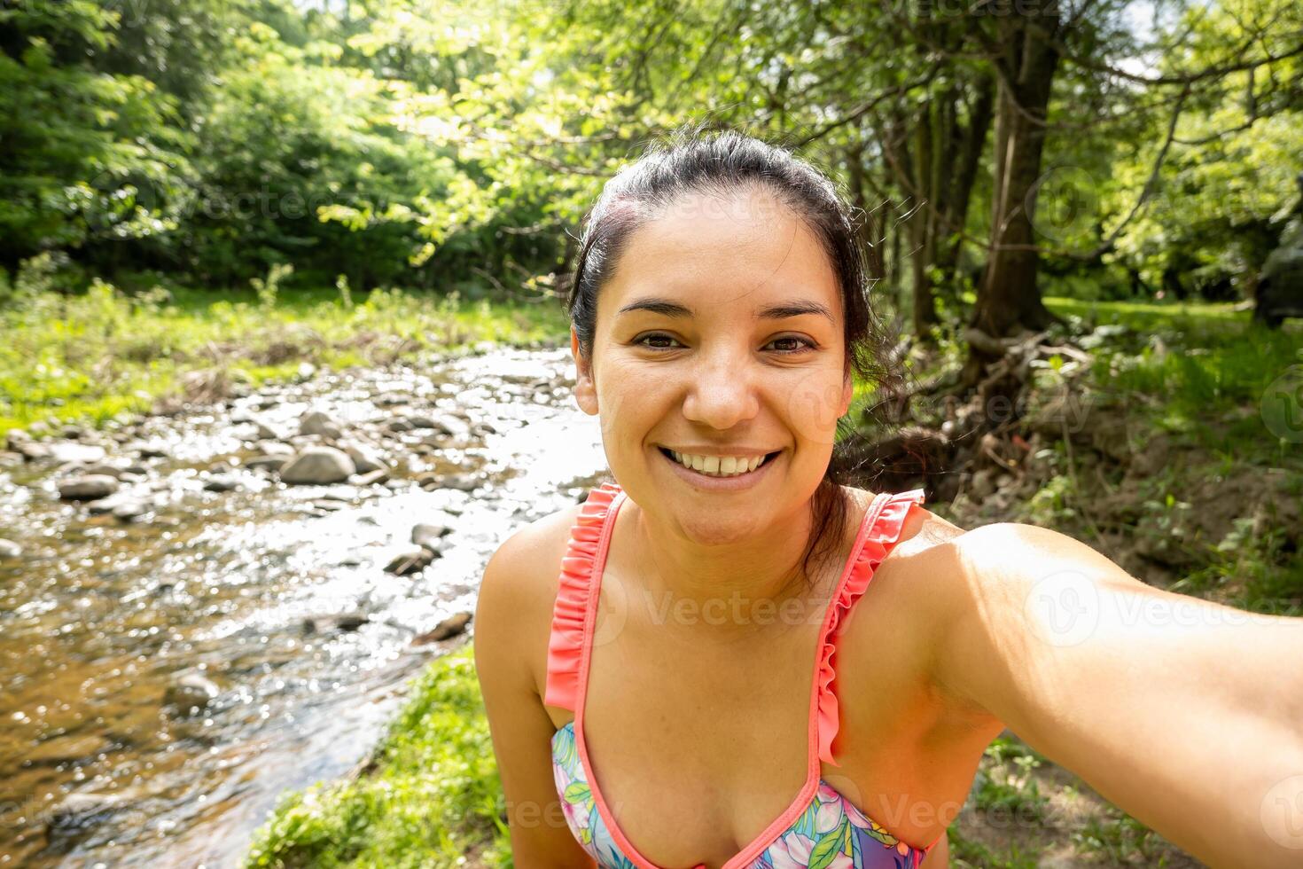 ung vuxen kvinna tar en leende selfie i en ström i Cordoba, argentina. hon är en turist bär en färgrik bikini. foto