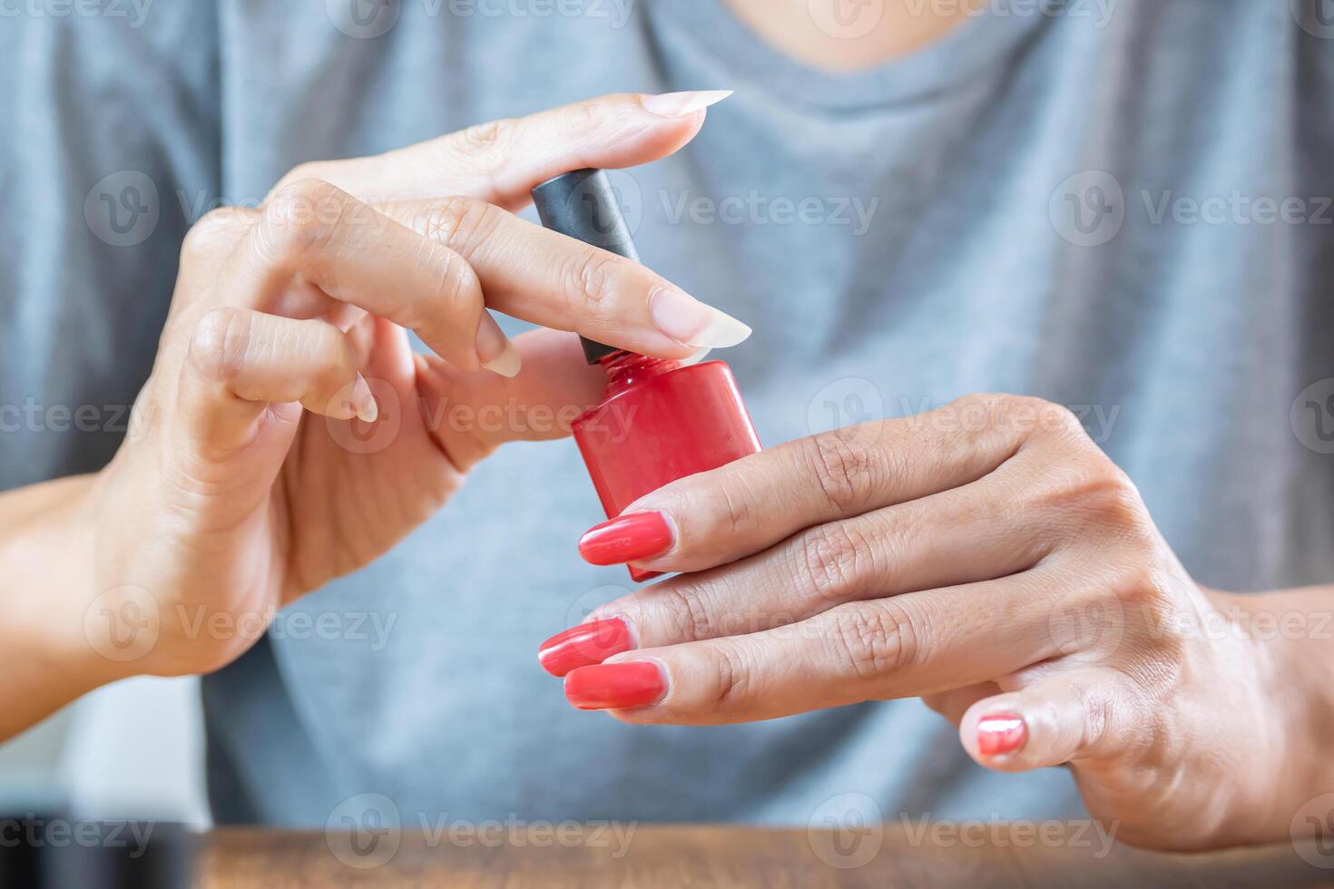 kvinna innehav en flaska av röd semipermanent nagel putsa. hon har ett hand med målad naglar och de Övrig inte. foto