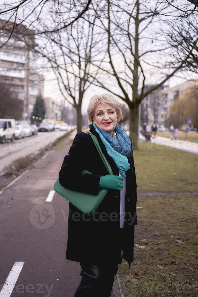 porträtt av en eleganta gammal kvinna i en svart täcka med grön Tillbehör på en vår gata foto