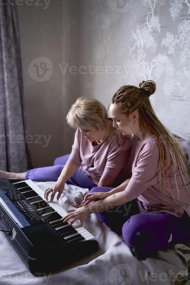 en 60-åring mor och en 40-åring dotter spela de tangentbord tillsammans på de säng på Hem foto