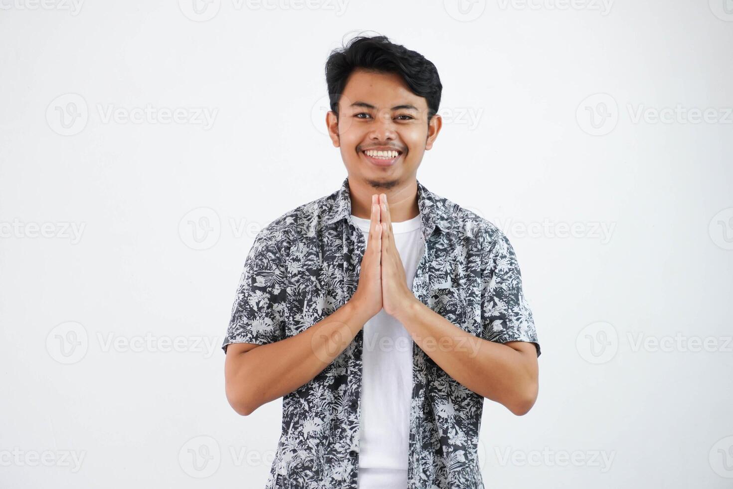 leende ung asiatisk man både händer tillsammans över hans bröst, uttrycker respekt och tacksam stående ser kamera isolerat på vit bakgrund foto