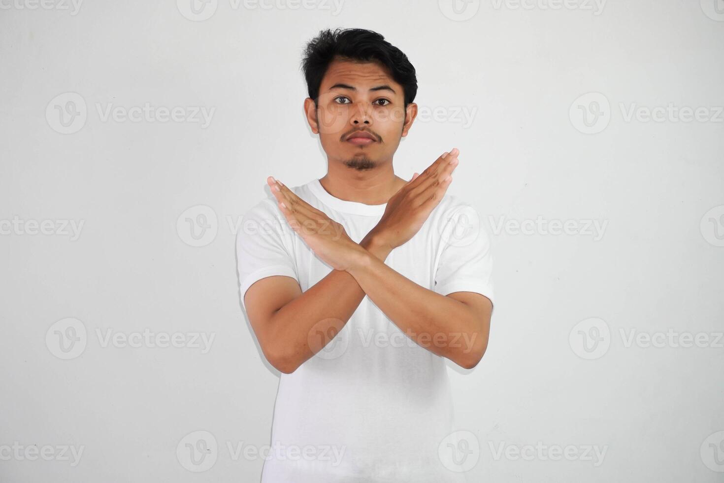 allvarlig ung asiatisk man bär vit t skjorta visa korsa vapen för instämmer inte alls säga Nej isolerat på vit bakgrund foto