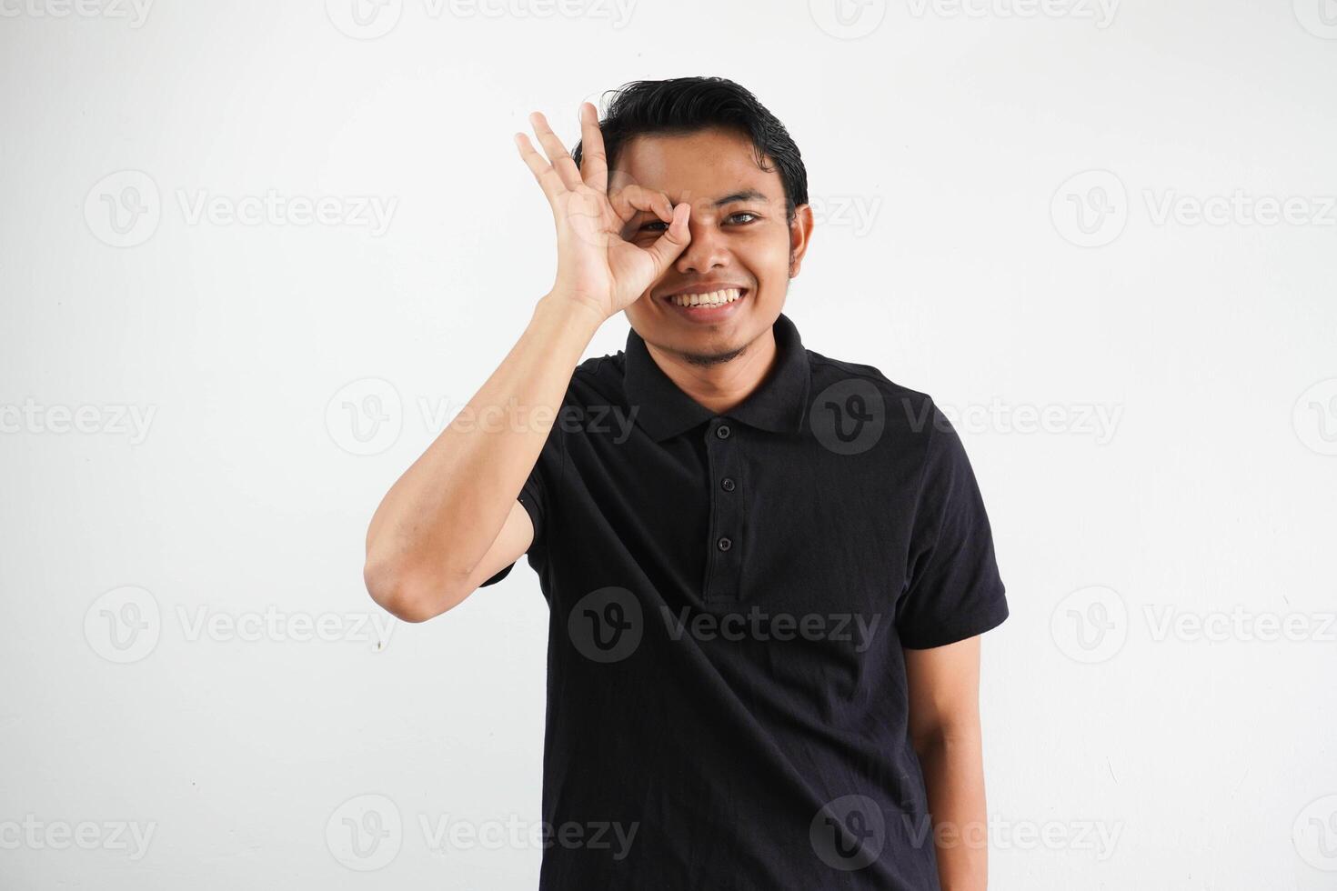 ung asiatisk man upphetsad förvaring ok gest på öga, bär svart polo t skjorta isolerat på vit bakgrund foto