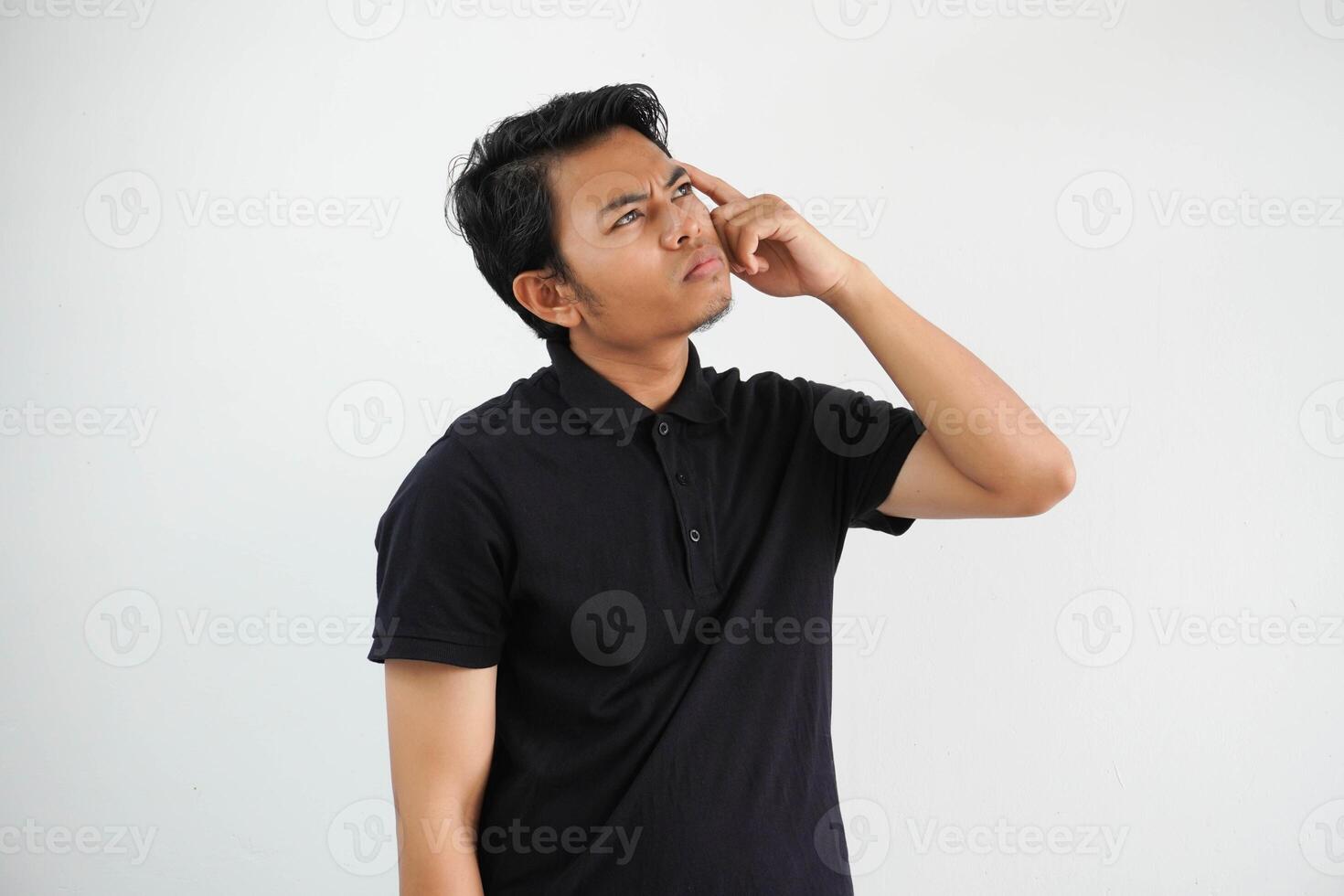 tänkande något aning ung asiatisk man och hand innehav huvud tillfällig utrusta svart polo t skjorta isolerat på vit bakgrund foto