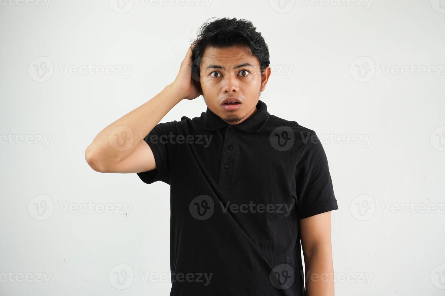 förvånad ung asiatisk man ser kamera bär svart polo t skjorta isolerat på vit bakgrund foto