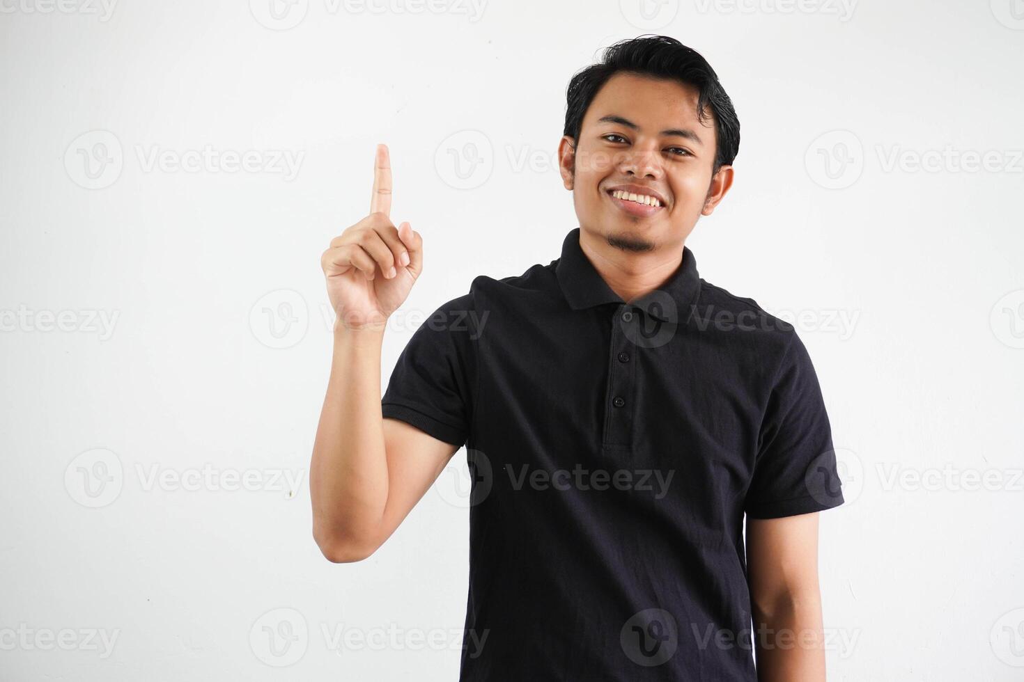 leende ung asiatisk man pekande upp med Lycklig ansikte uttryck bär svart polo t skjorta isolerat på vit bakgrund foto