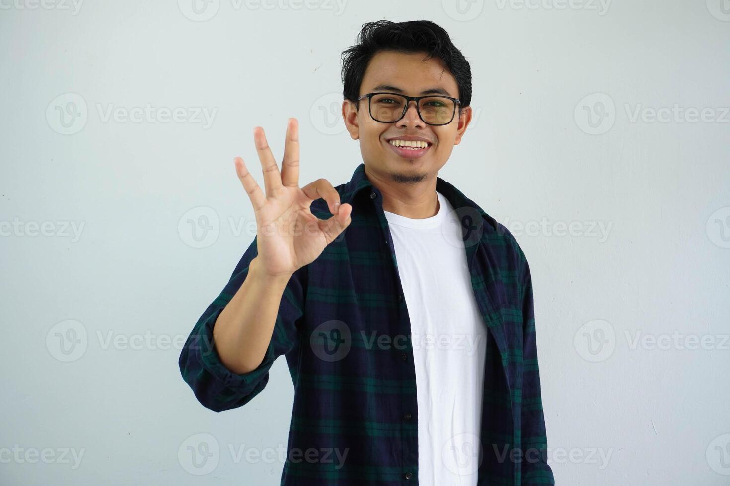 ung asiatisk man som visar upphetsad ansikte uttryck medan ger ok finger tecken isolerat på vit bakgrund. foto