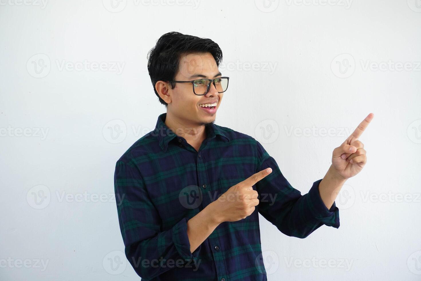 leende ung asiatisk man ser och pekande till de vänster sida med både händer isolerat på vit bakgrund foto