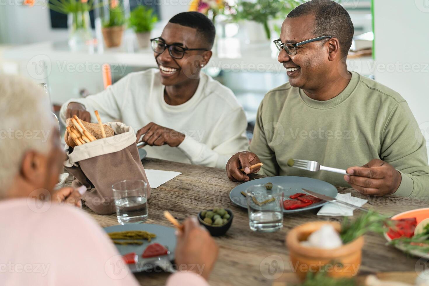 Lycklig afro latin familj äter friska lunch med färsk grönsaker på Hem - mat och föräldrar enhet begrepp foto