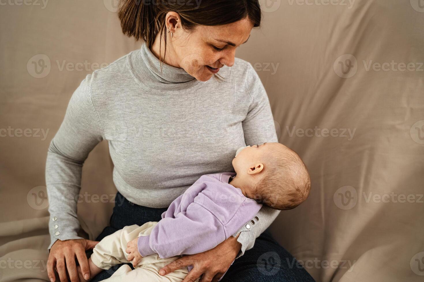 Lycklig mor tar vård av henne små bebis sovande i henne vapen på Hem - begrepp familj och moderskap foto