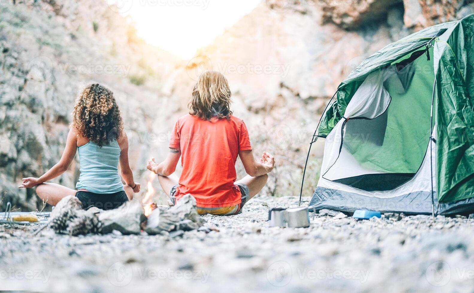 hälsa ung par håller på med yoga Nästa till brand medan camping med tält på en berg - vänner mediterar tillsammans på stenar på solnedgång - människor, hälsa, livsstil och sporter begrepp foto