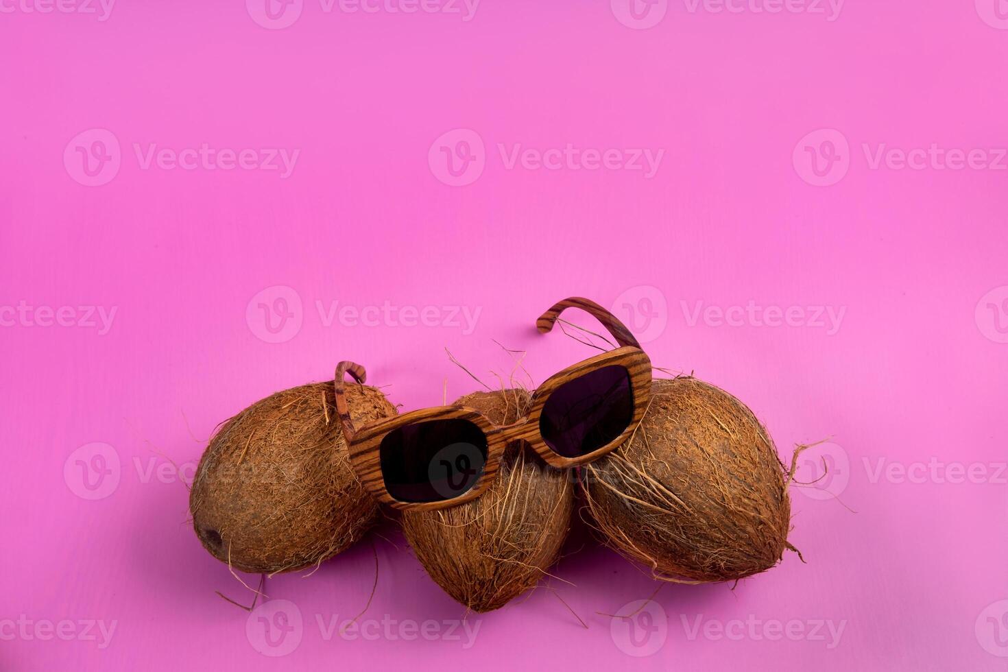 tre hela kokosnötter och trä- glasögon på en rosa bakgrund foto