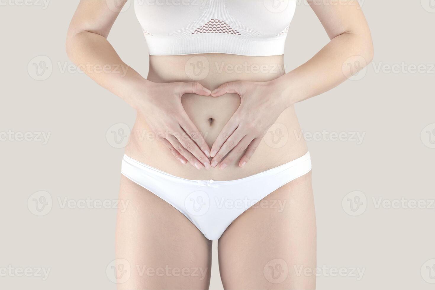 kvinna i underkläder innehav händer på henne mage framställning en hjärta symbol, kvinnors hälsa vård. begrepp av skönhet, kropp och hud vård, medicin eller graviditet foto