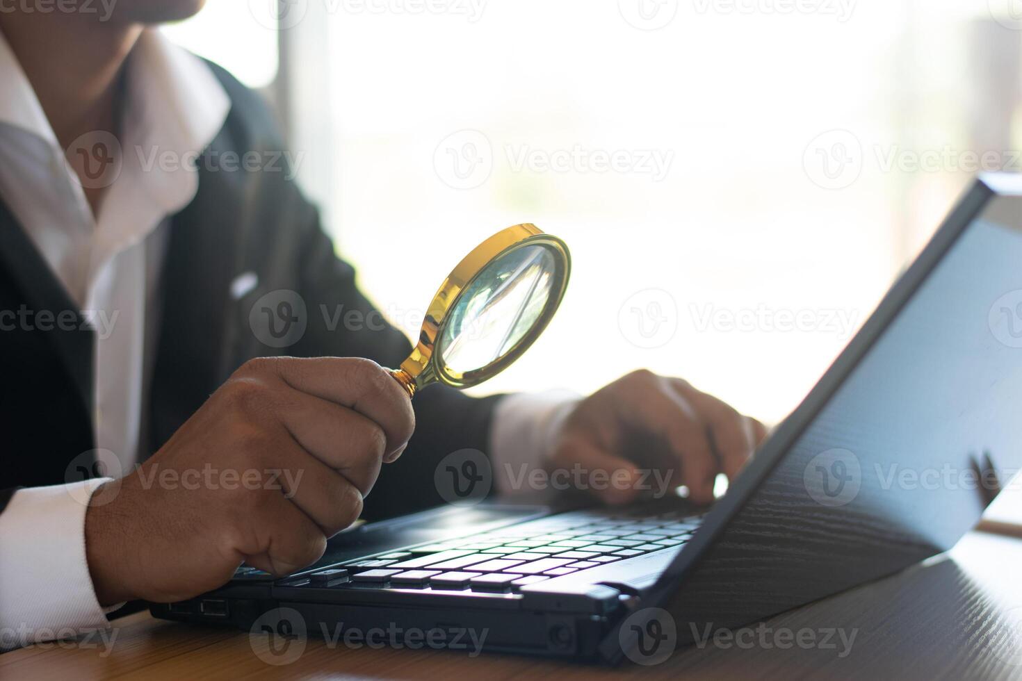en affärsman eller revisor Arbetar på en dator och användningar en förstorande glas till se på företag dokument på de kontor tabell. foto