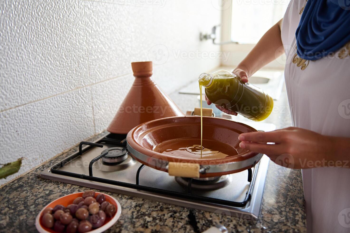 närbild hemmafru början matlagning måltid i tajine lera pott, häller extra jungfrulig oliv olja inuti en lera maträtt foto