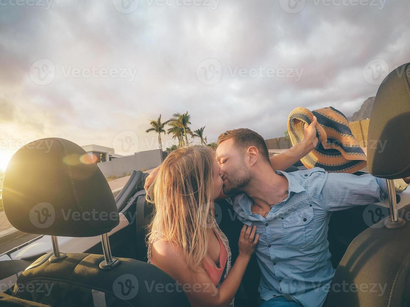 Lycklig ung par har kissing i konvertibel bil under deras väg resa - trendig romantisk älskande har en anbud ögonblick i cabriolet bil - kärlek, relation och resa transport livsstil foto