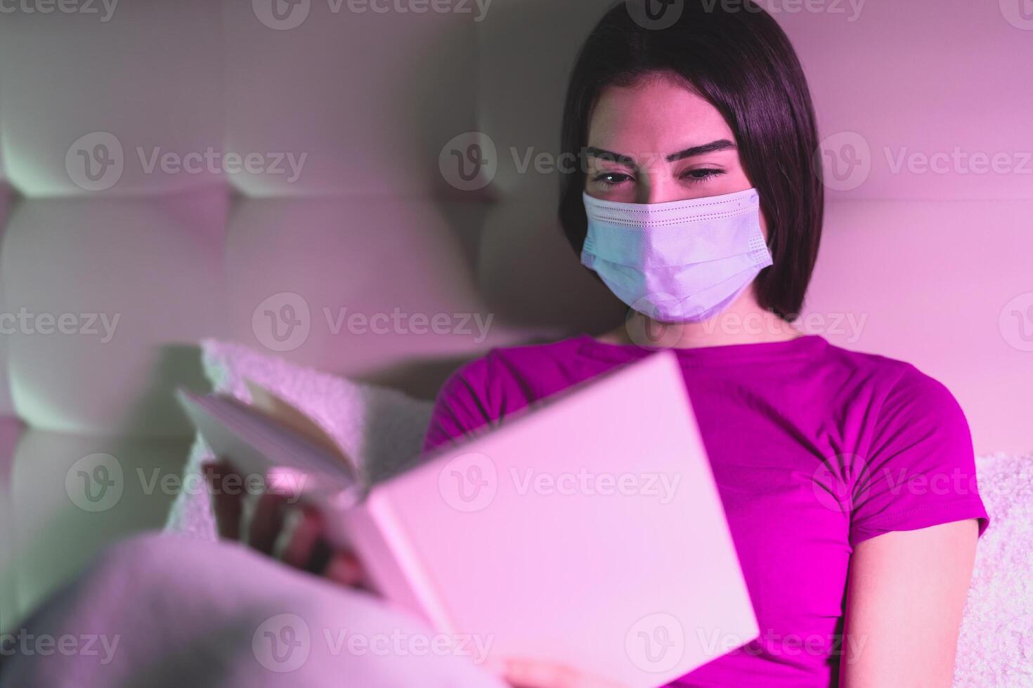 ung kvinna bär kirurgisk mask läsning bok i säng - hälsa mental påverkan korona virus spridning - healtcare människor och covid19 förlossning begrepp foto