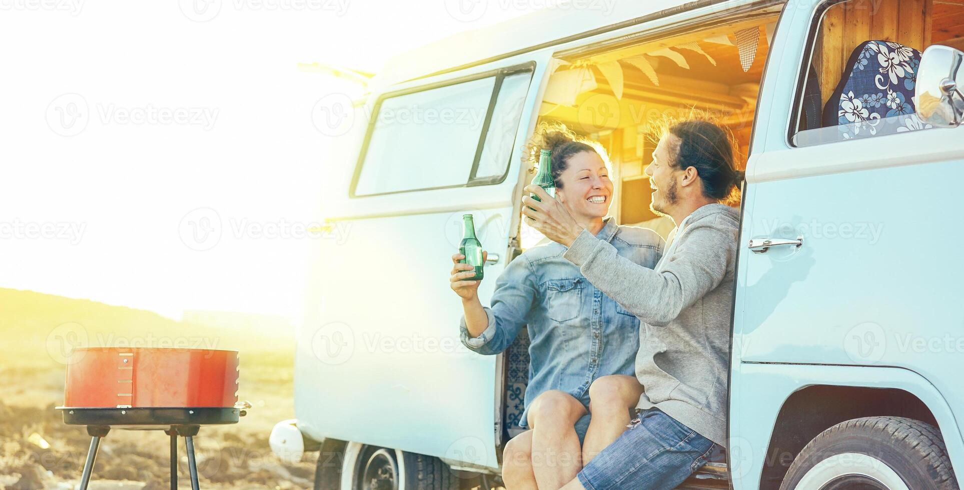 resa par har roligt dricka öl Sammanträde på deras årgång husbil mini skåpbil - Lycklig människor med deras sällskapsdjur njuter utegrill på solnedgång under en bilresa - begrepp av semester livsstil och kärlek foto