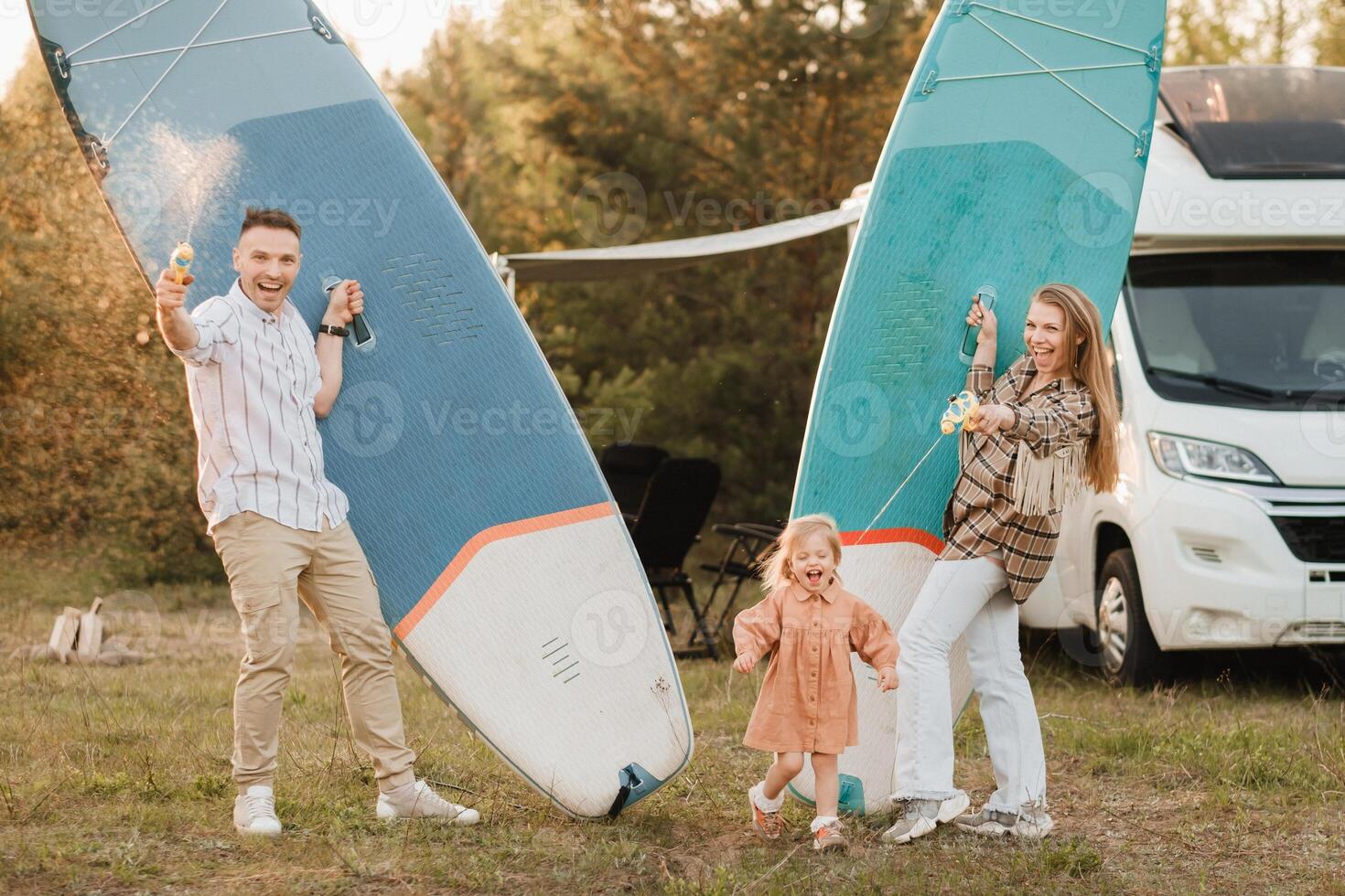 de familj är vilar Nästa till deras mobil Hem. pappa, mamma och dotter spela med supera styrelser och vatten pistoler nära en mobil Hem foto