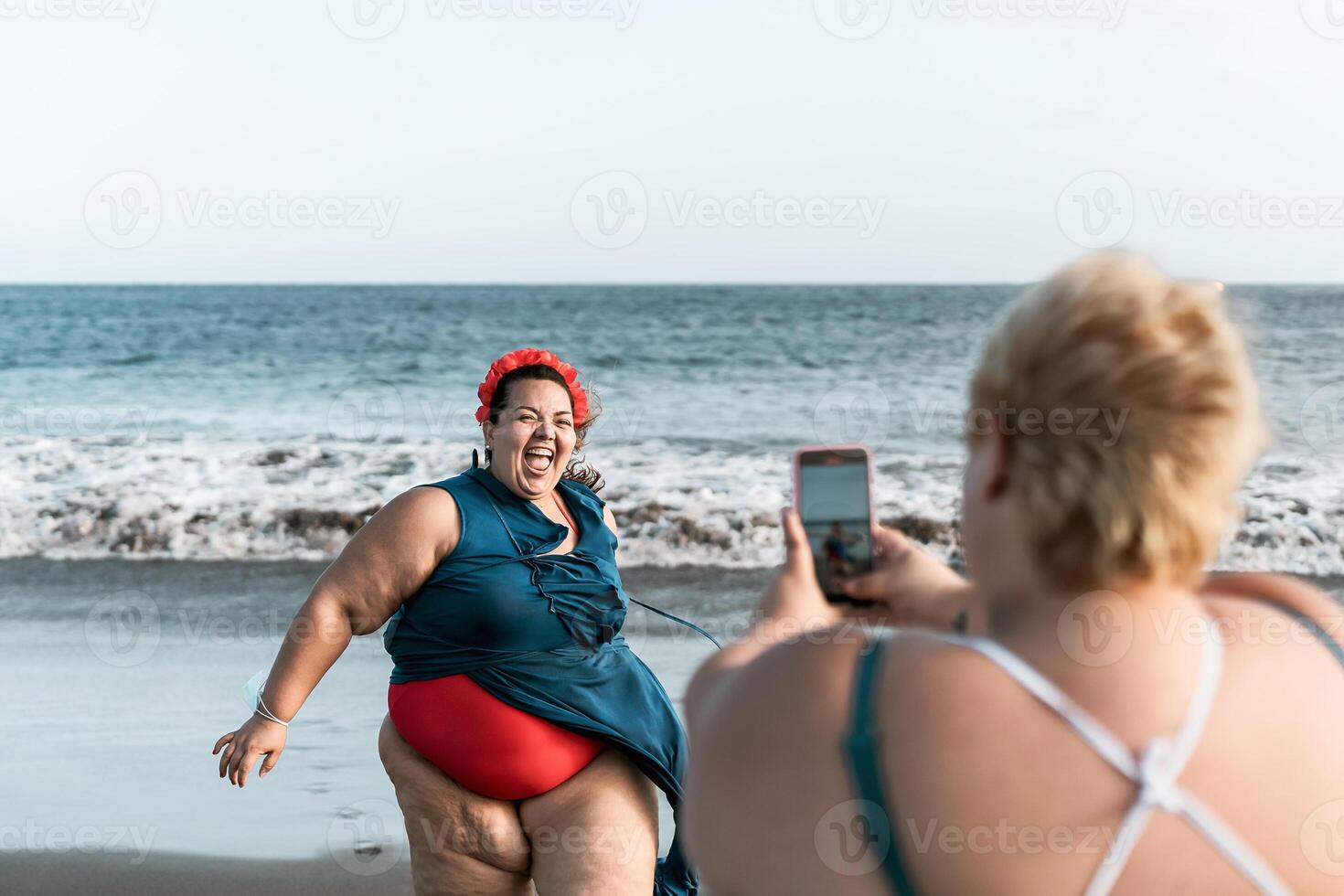 Lycklig plus storlek kvinnor har roligt framställning foton på de strand med mobil smartphone - övervikt självsäker människor livsstil och teknologi begrepp