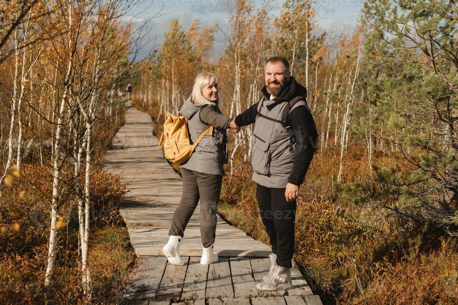 människor i stövlar promenad längs en trä- väg i en träsk i yelnya, Vitryssland foto