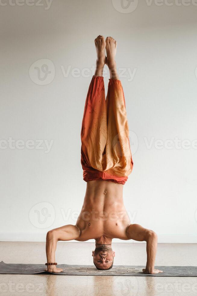 en man med en naken torso gör yoga stående på hans huvud inomhus. kondition tränare foto