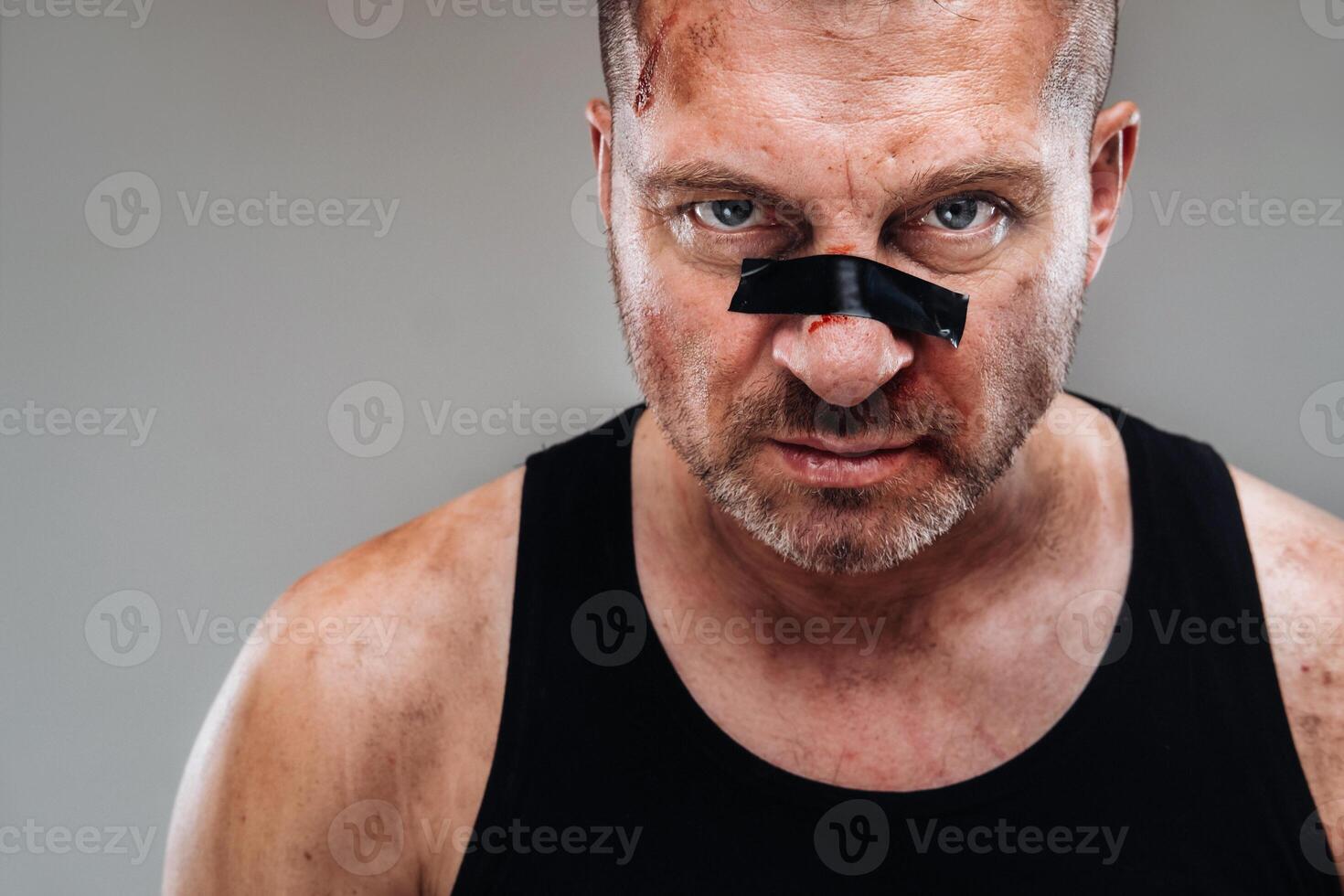 på en grå bakgrund står en misshandlade man i en svart t skjorta ser tycka om en kämpe och framställning för en bekämpa foto