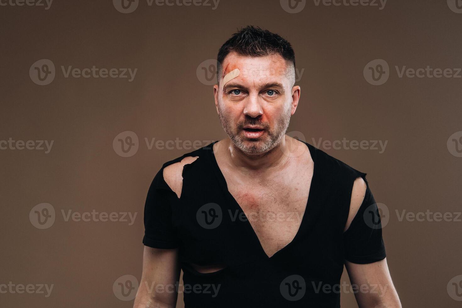 mot en grå bakgrund står en misshandlade arg man i en svart t-shirt med sår foto