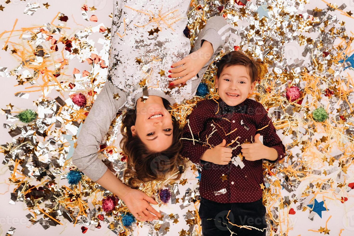 mor och son lögn på de golv i konfetti på en vit bakgrund. en kvinna och en pojke i konfetti på en vit bakgrund foto