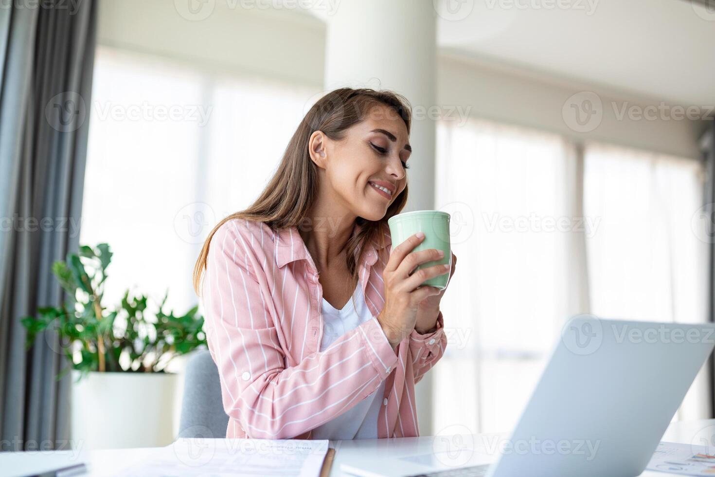positiv ung kvinna frilansare tittar på video i blog på netbook och har en kaffe på bekväm kontor. skön ung företag kvinna arbetssätt på laptop.frilansare ansluter till internet foto