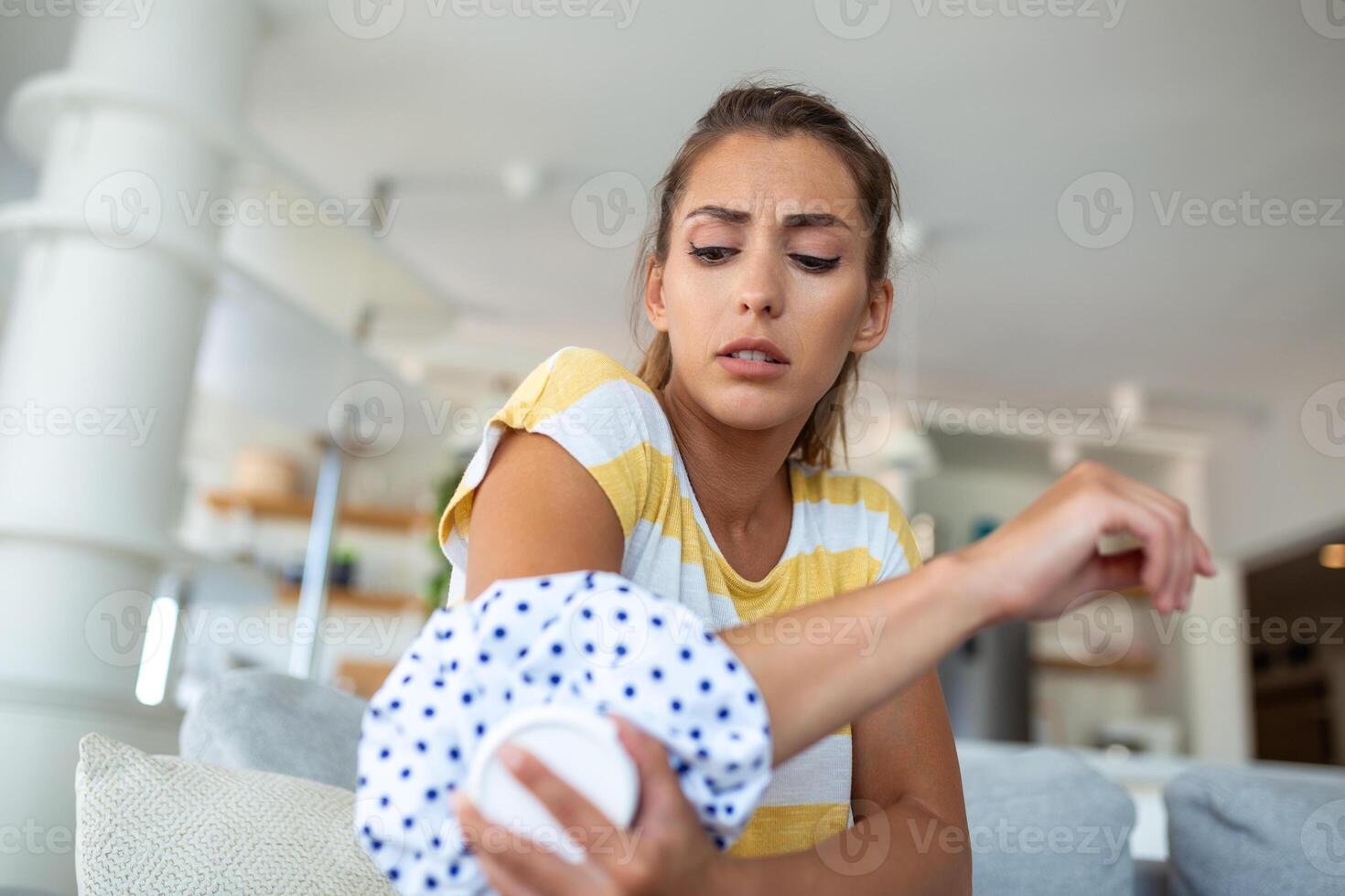 ung kvinna är Sammanträde på Hem på henne soffa och rörande de henne armbåge medan lidande från armbåge smärta, placering is packa på ont fläck foto