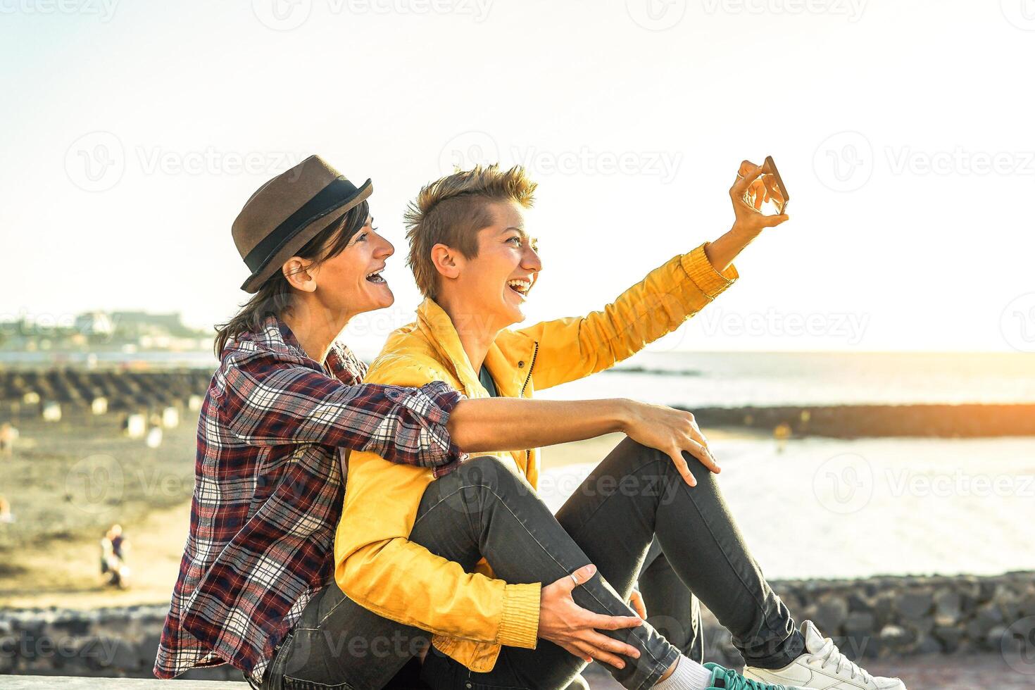 Lycklig Gay par tar en selfie med mobil smart telefon kamera på de strand på solnedgång - lesbiska har roligt i Semester - homosexualitet, mångfald, semester, resa, HBTQ, teknologi begrepp foto