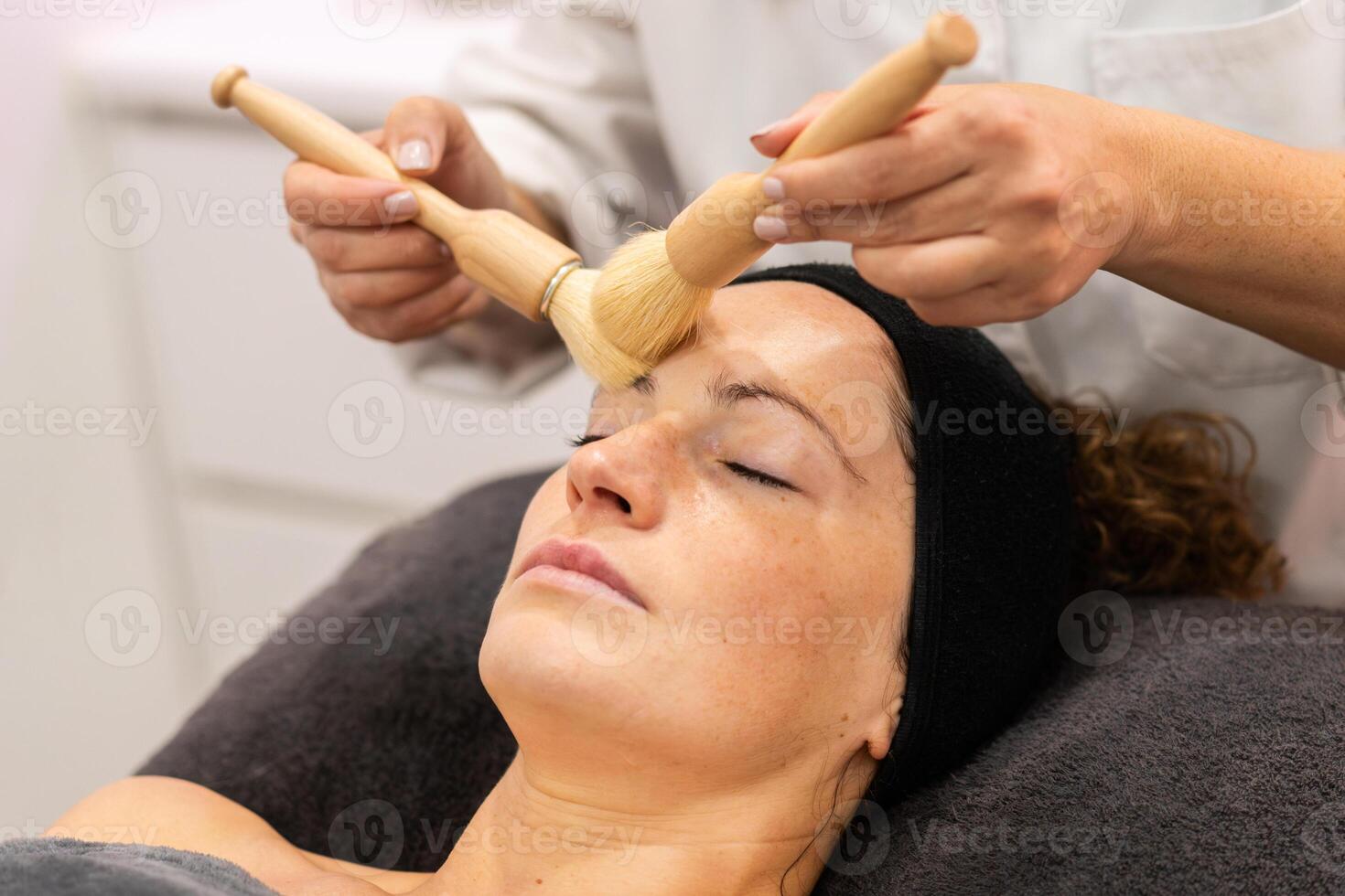 beskära professionell kosmetolog rengöring ansikte av kvinna klient med borstar i skönhet salong foto