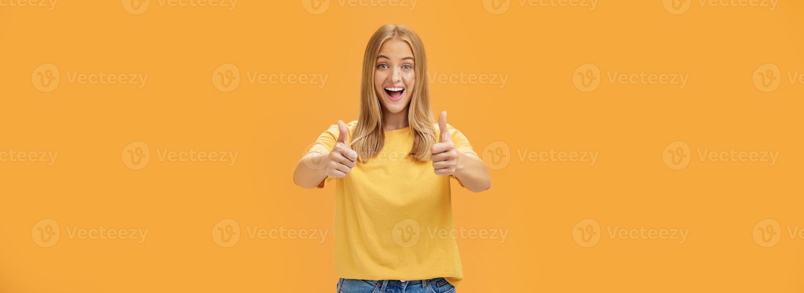 kvinna stöder med Uppfostrad tummen upp och roade glad leende som visar positiv attityd uttrycker tycka om på begrepp eller aning ger godkännande Framställ Lycklig och förtjust mot orange bakgrund foto