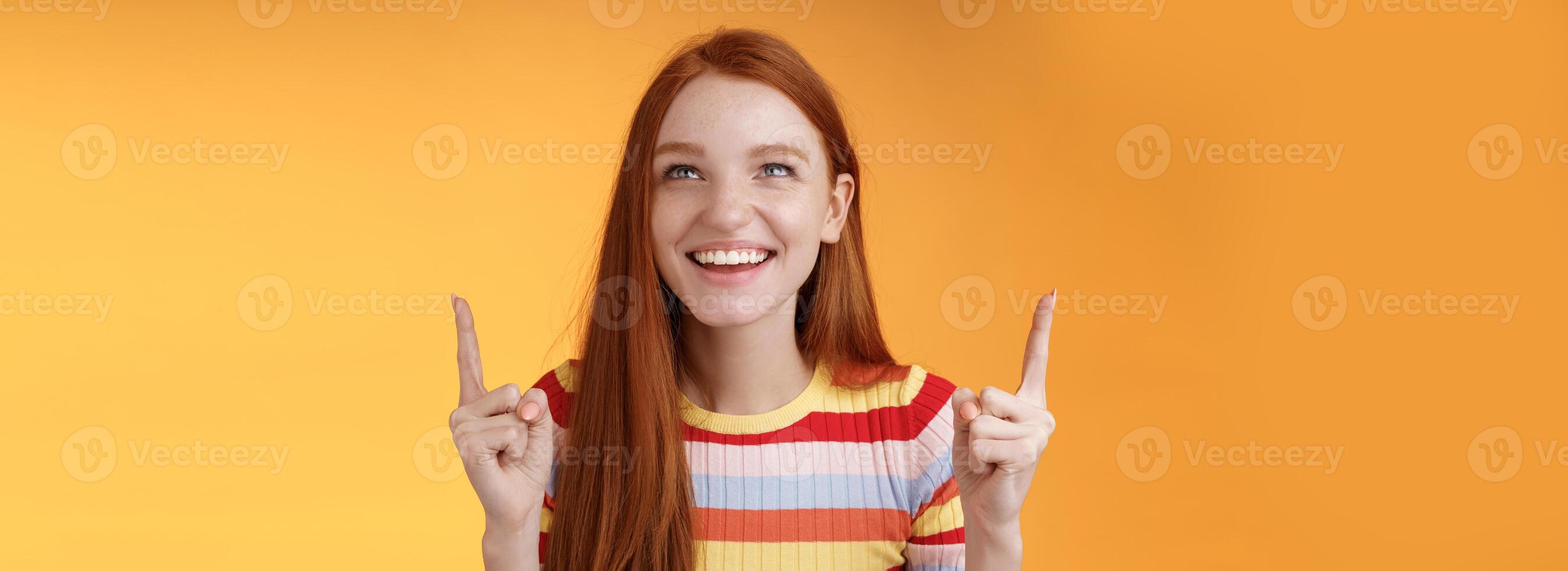 Lycklig glad rödhårig flicka har roligt nöje parkera skrattande glatt pekande se upp index fingrar uppåt njut av underhållning stående orange bakgrund roade flin glatt foto