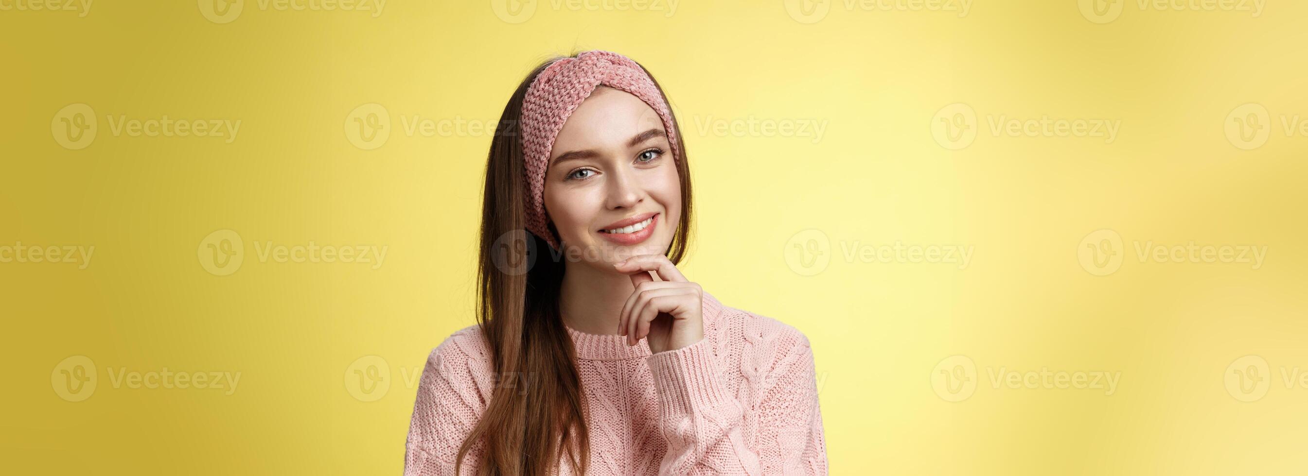 Lycklig ung europeisk kvinna i stickat pannband, Tröja lutande huvud rörande haka och leende dumbom, tar vård av hud, känsla ansikte glittrande ser klar och friska efter hudvård behandling foto