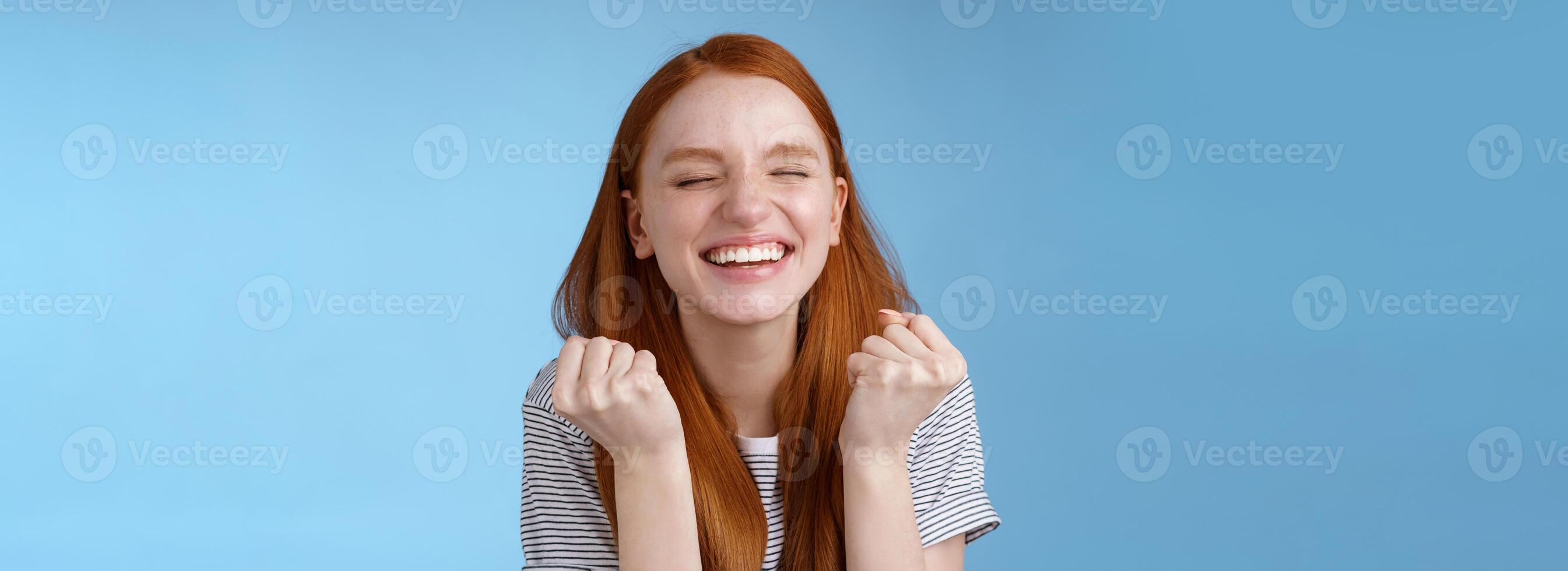 Lycklig skicklig snygg ingefära flicka motta positiv resultat testa knyta nävar fröjd skrikande ja fira do vinnare dansa stänga ögon lättad stående blå bakgrund triumferande foto