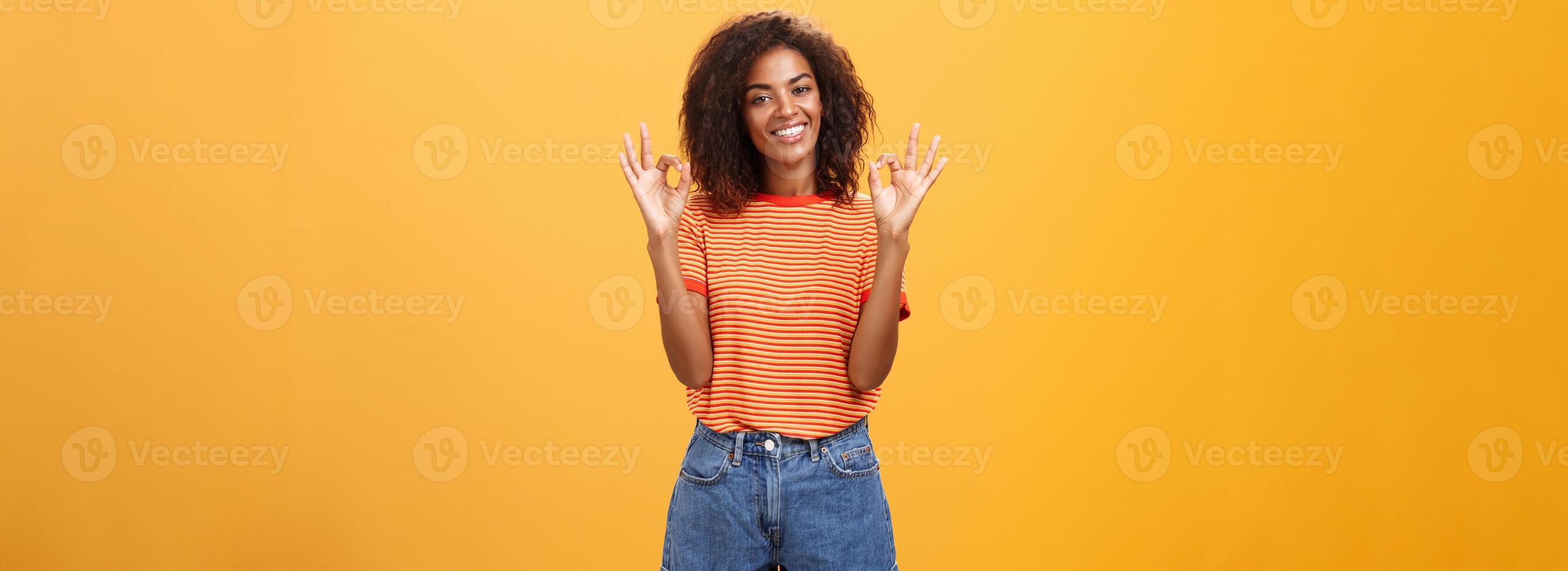 kyla attraktiv nöjd afrikansk amerikan kvinna kund plockning ny utrusta varelse förtjust och nöjd med Häftigt personal höjning händer i Okej eller grymt bra gest leende lyckligt över orange vägg foto