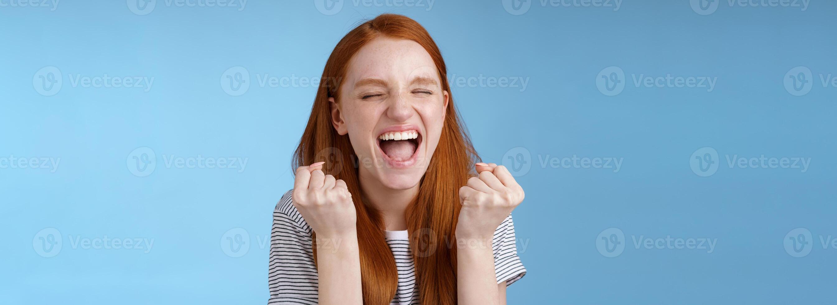 ja prestation mål livstid. leende Lycklig europeisk rödhårig flicka höjning knöt nävar glad fröjd skrikande ja utföra mål Framgång triumferande seger, bra Nyheter vinna lotteri foto