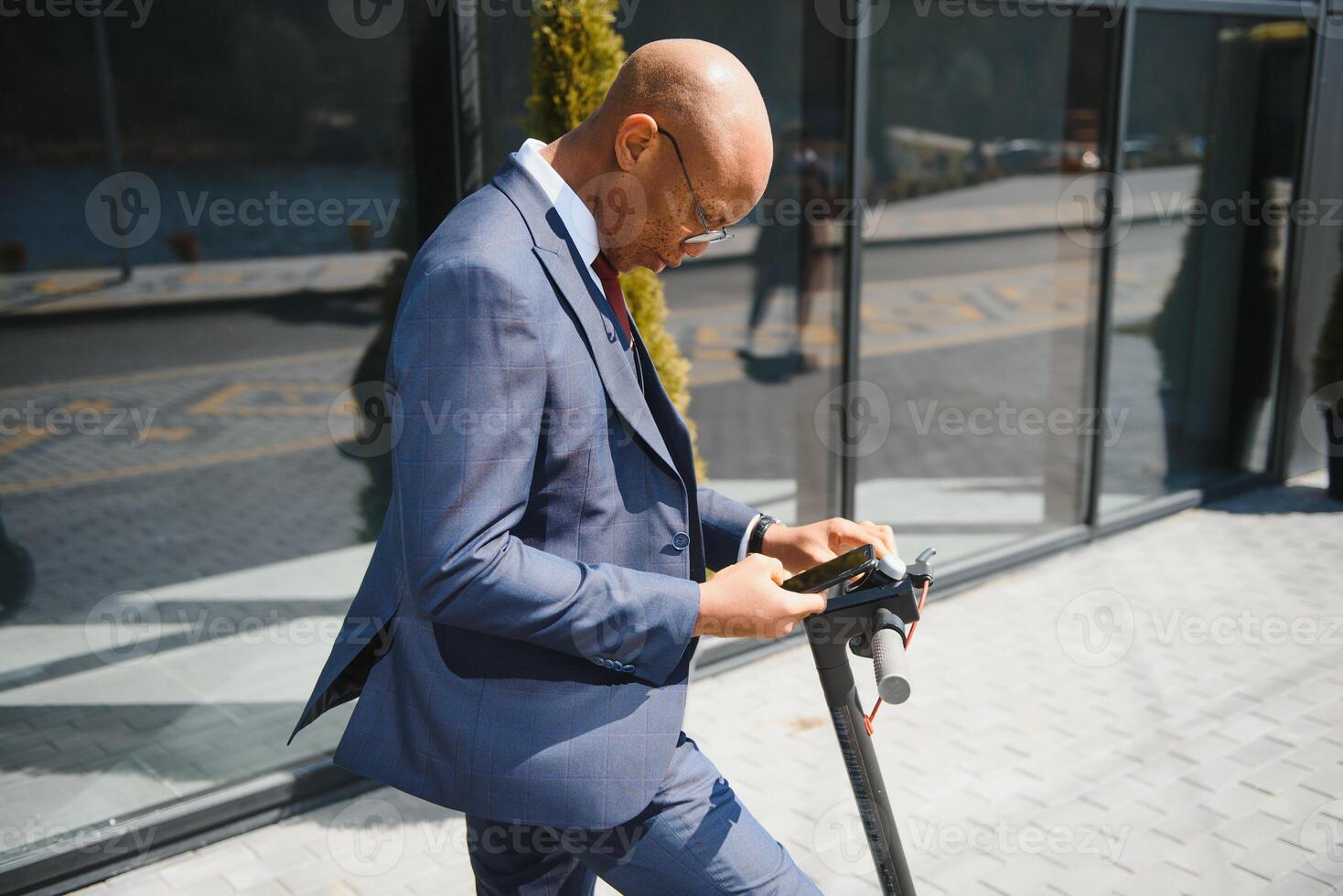 Lycklig afro 30s man kontroll hans telefon under e-skoter rida i stor stad foto